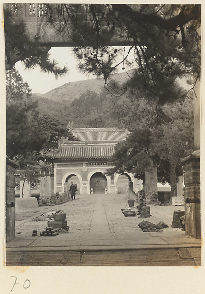 View through the archway of a pai lou at Tan zhe si showing a courtyard with stelae, a market, and a temple gate