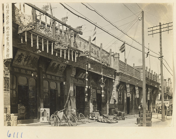 View of shopfronts showing shop signs for a paint and dye shop (left) and a metal-work shop (center)