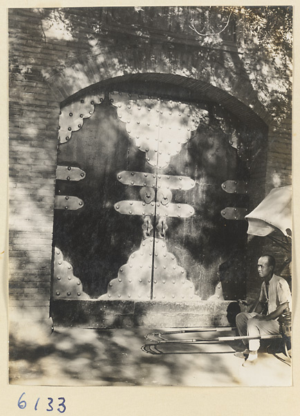 Rickshaw puller seated in front of a door with with brass decorations