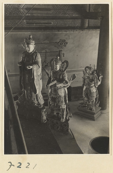 Temple interior at Jie tai si showing three shrine figures and a bell suspended from a frame in the background