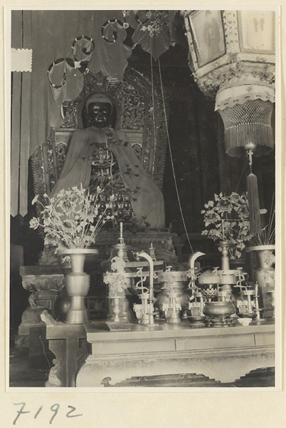 Interior of a temple building at Jie tai si showing an altar with draped statue of Buddha, ritual objects, and a lantern