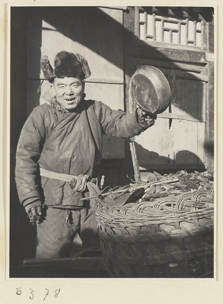 Itinerant charcoal seller holding a drum or gong next to basket of charcoal