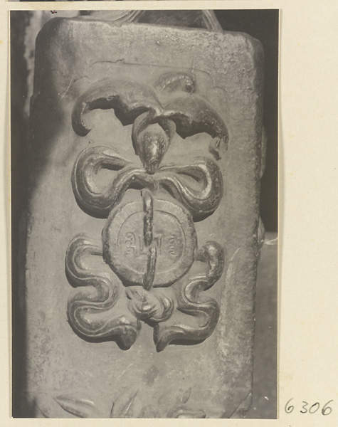 Carved door stone with bat, knot, and coin motifs