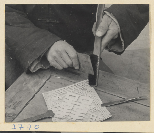 Paper-cut maker brushing soot through a paper-cut to transfer the pattern to a new sheet of paper