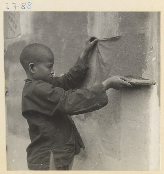 Boy hanging sheets of paper on a wall to dry outside paper-making shop