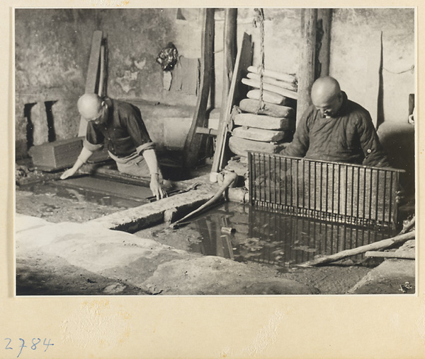 Two men working with vats of paper pulp in a paper-making shop