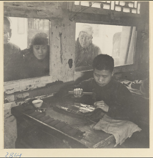 Passersby watching a silversmith at work in a shop