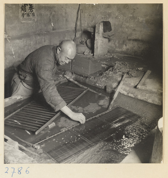 Man placing screens in a vat of paper pulp in a paper-making shop