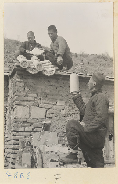 Men demonstrating how roof tiles fit together on the roof of a tile and brick factory near Mentougou Qu