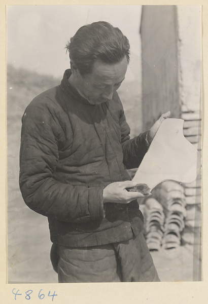 Man inspecting roof tile at a tile and brick factory near Mentougou Qu