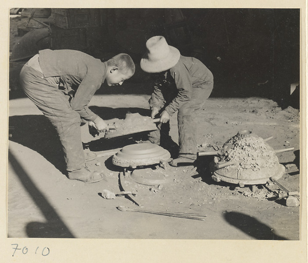 Boys removing an iron pot from a mold at a foundry near Mentougou Qu