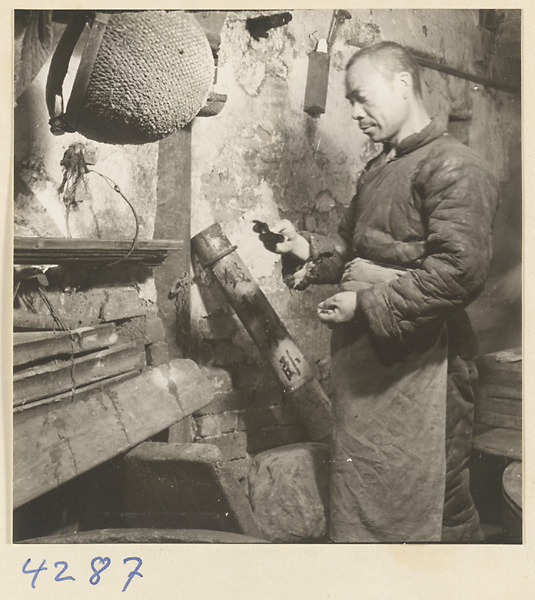 Man at work in a tofu-making shop next to a reed water bucket and a bamboo money tube