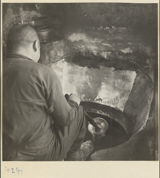 Man stirring sesame oil in a metal vat in a sesame oil shop