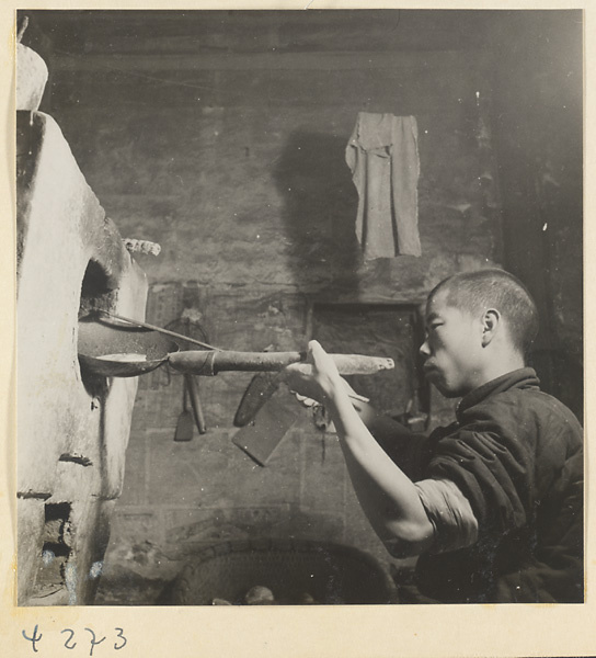 Kitchen interior showing a baker at an oven holding a pan with a ma bing