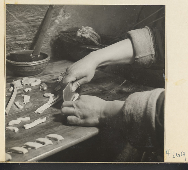 Kitchen interior showing a man lengthening pieces of dough to make oil cakes