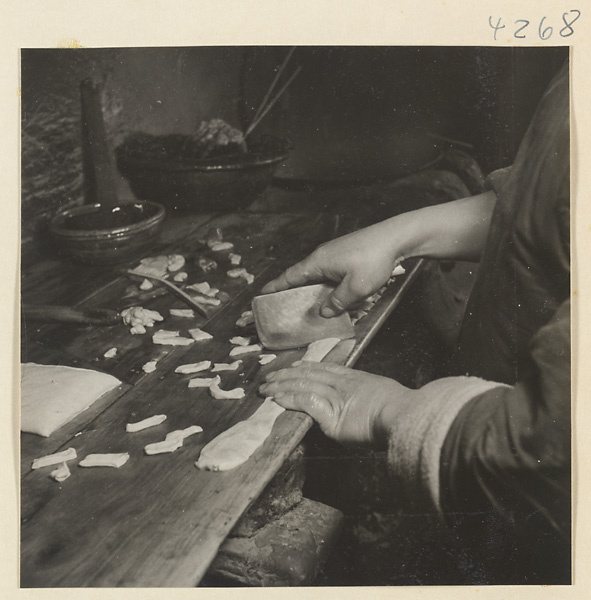 Kitchen interior showing a man cutting dough into pieces to make oil cakes