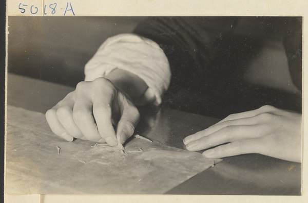 Interior of a scroll-mounting shop showing a man removing the old paper backing from a scroll painting