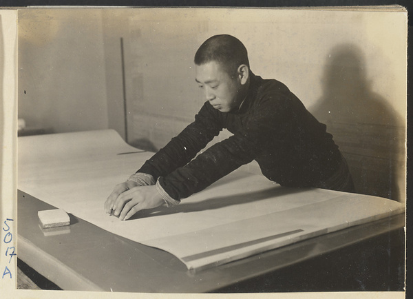 Interior of a scroll-mounting shop showing a man burnishing the back of scroll with a polishing shell called a ya luo to facilitate the rolling and unrolling of the scroll