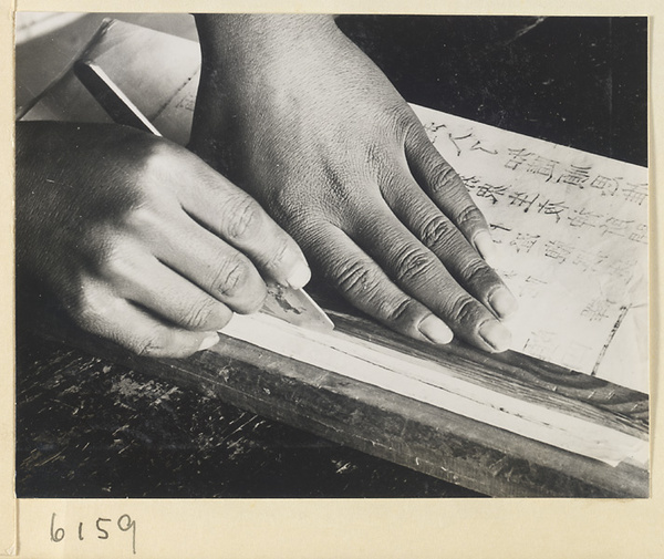 Monk trimming the edges of a printed sheet in the printing room of a Buddhist temple