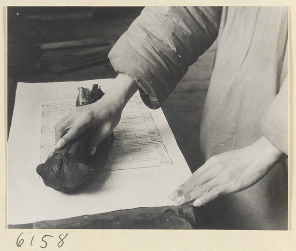 Monk impressing a piece of paper on an inked printing block in the printing room of a Buddhist temple