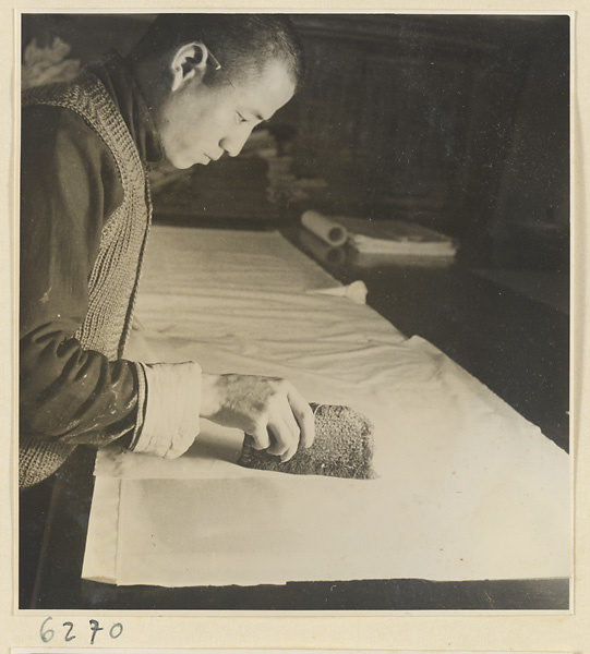 Interior of a scroll-mounting shop showing a man brushing a backed scroll painting with a stiff brush called a zhong pi shua