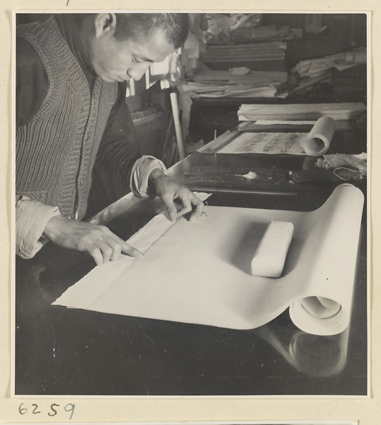 Interior of a scroll-mounting shop showing a man working on the edge of a scroll