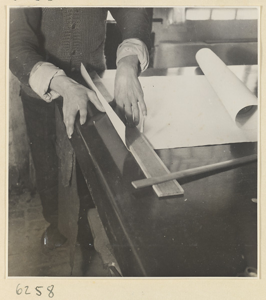 Interior of a scroll-mounting shop showing a man working on the edge of a scroll
