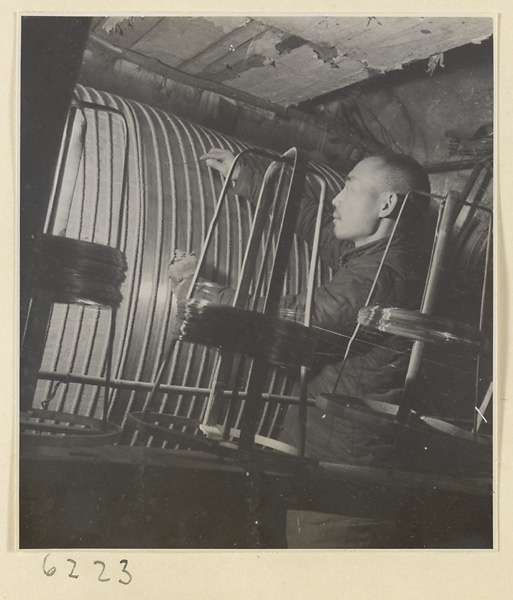 Interior of copper-net factory showing a man working with rolls of copper wire