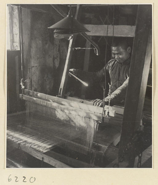 Interior of copper-net factory showing a man working at a loom