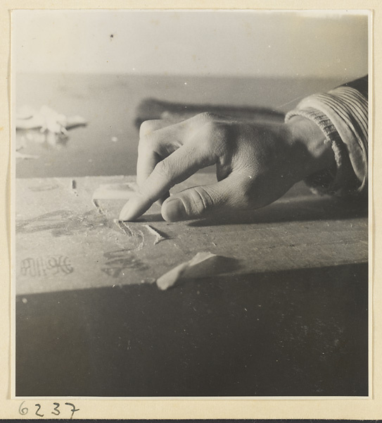 Interior of a scroll-mounting shop showing a man removing the old backing from a scroll painting