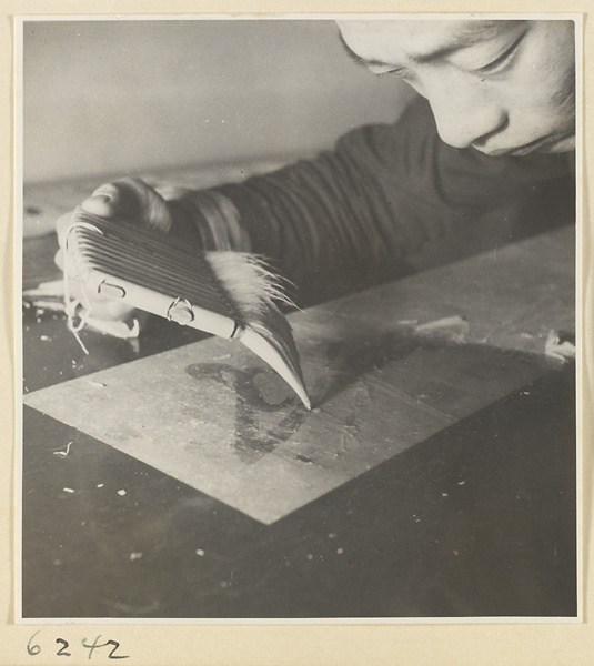 Interior of a scroll-mounting shop showing a man using a soft brush called a shui shua to moisten the back of a scroll to remove the old paper backing