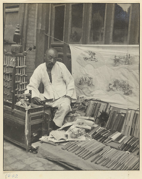 Fan vendor displaying fans, banner with samples of fan paintings, and strings of bells called chuan ling