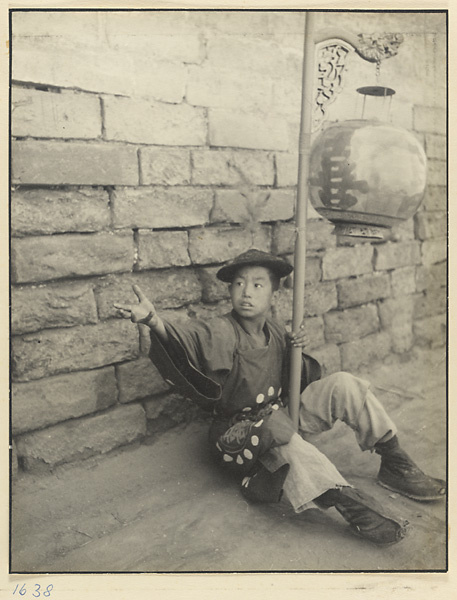 Seated boy in ceremonial dress holding wedding lantern inscribed with characters for double happiness