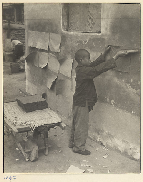 Boy pasting sheets of newly-made coarse paper on a wall to dry
