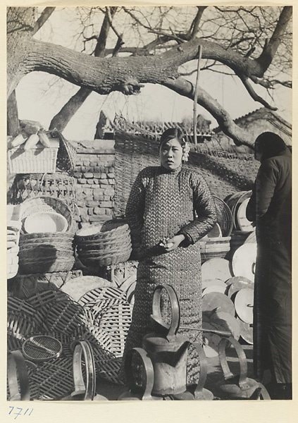 Woman standing next to a vendor's stand that sells baskets and household goods at Longfusi Market