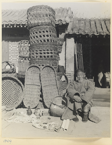 Man hawking decorative objects, beads, and jewelry in front of a basket shop