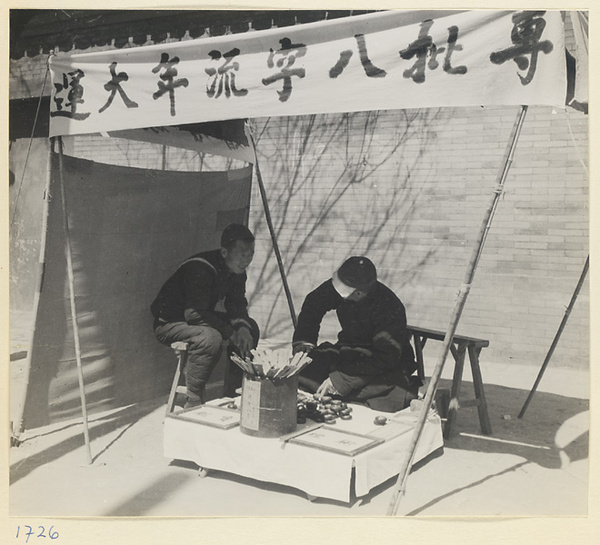 Fortune teller with his divination tools sitting under a banner advertising his services