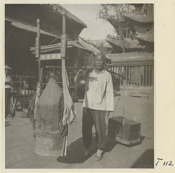 Itinerant repairman who fixes umbrellas carrying boxes suspended from a shoulder pole on a street in Tai'an