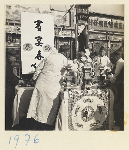 Curbside altar with hanging scroll set up in front of a paint and dye shop during a funeral