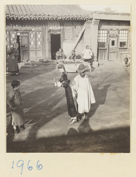 Spectators watching member of a funeral procession carrying a paper figure of a male servant