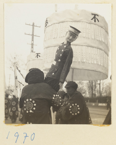 Members of a funeral procession carrying a paper figure of a policeman and an umbrella with inscriptions