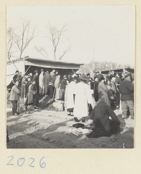 Members of a funeral procession outside a mat shed