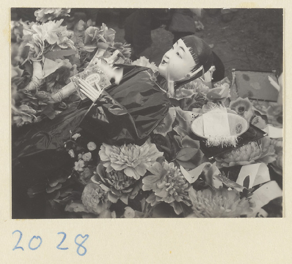 Paper figure of a servant and a bowl lying amidst paper flowers during funeral