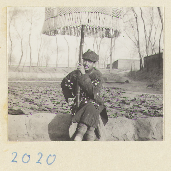 Member of a funeral procession sitting holding an umbrella outside a city