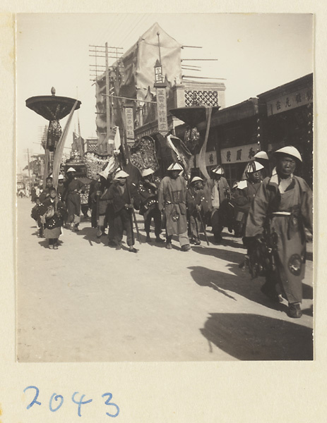 Members of a wedding procession carrying furled umbrellas and fan-shaped screen