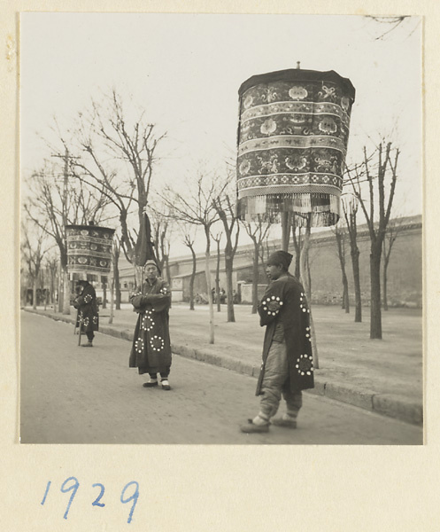 Members of a funeral procession with umbrellas and flag