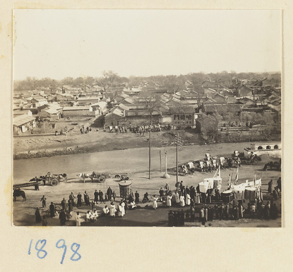 Members of a funeral procession holding umbrellas and banners with city moat and houses in background