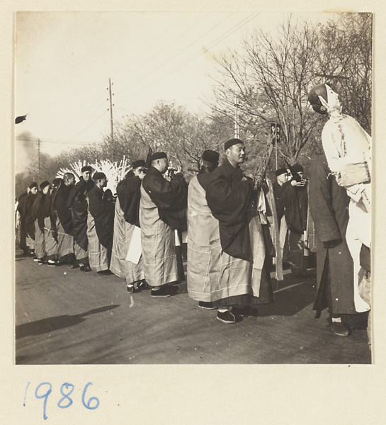 Man carrying paper figure and Buddhist monks playing instruments in a funeral procession