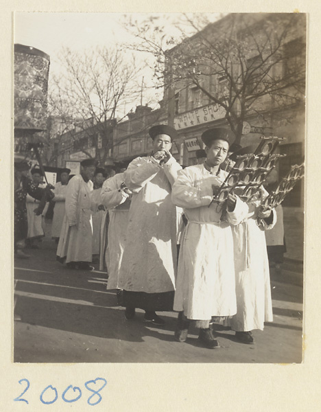 Musicians dressed in white playing musical instruments including yun luo during funeral procession