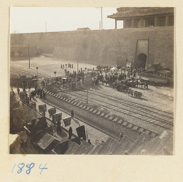 Funeral procession with umbrellas passing through a city gate